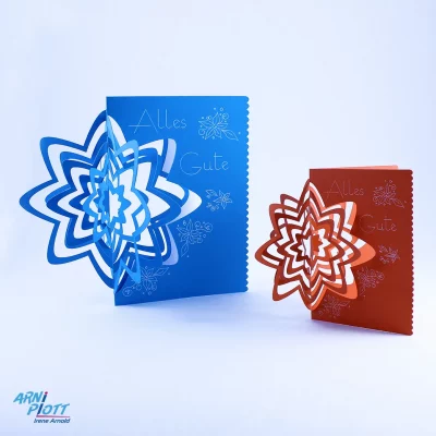 Zwei stehende Pop-up Karten mit einer 3D Blume in Blau und Orange mit weißen Verzierungen und weißer Aufschrift Alles Gute - nach einer Plotterdatei von ARNi-Plott
