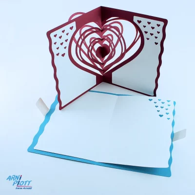 Aufgeschlagene blaue Popup-Karte mit weißem doppelseitigem Einlegerblatt und eine rote stehende Pop-up-Karte mit einem aufgefächerten Herzen und eingeklebten Einlegeblättern - Plotterdatei von ARNi-Plott